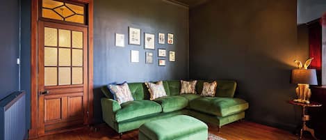 A room with a green sofa, a patterned rug, a wooden door with glass panels, and a chandelier.