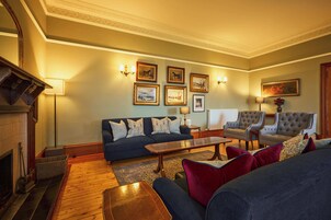 Un salón tradicional con un sofá azul oscuro, una mesa de centro de madera y dos sillones.