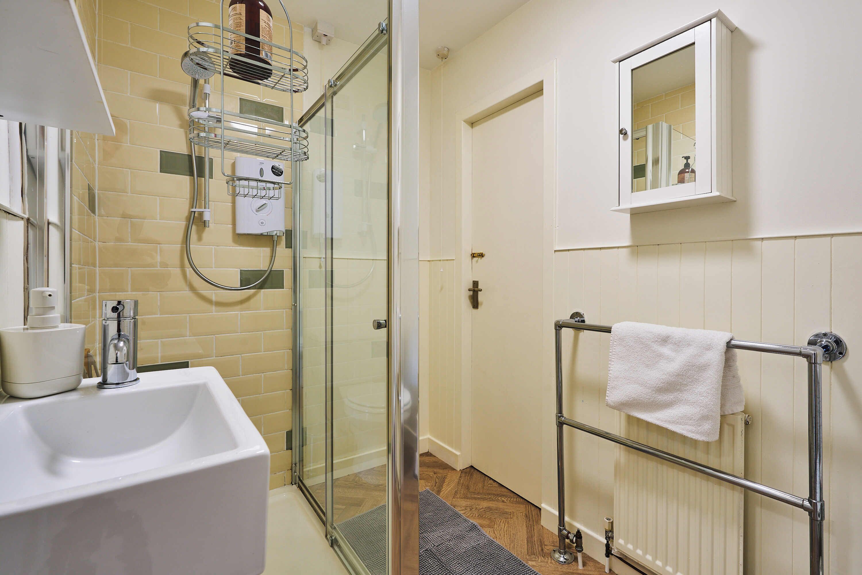 Une salle de bain avec une douche à parois de verre, un lavabo blanc, un porte-serviettes et un miroir.
