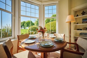Comedor con una mesa redonda dispuesta para cuatro personas, sillas alrededor y vista a un jardín a través de amplias ventanas.