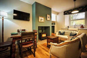 Una sala de estar acogedora con chimenea, una mesa de comedor con sillas, un sofá con cojines decorativos y un televisor montado en la pared.