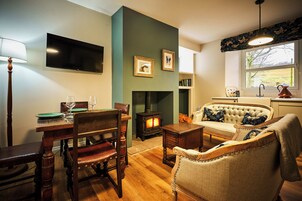 Una sala de estar acogedora con chimenea, una mesa de comedor con sillas, un sofá con cojines decorativos y un televisor montado en la pared.