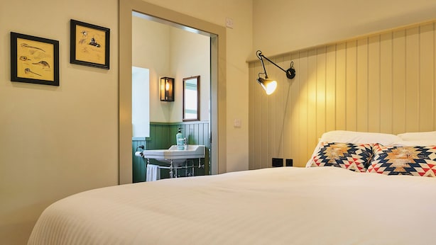 A bedroom with a large bed, a nightstand, a wall-mounted lamp, and framed artwork on the wall. - Kinclune House & Cottages - Sleeps 28 (Kirkton of Kingoldrum)