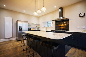 Cocina moderna con una isla central, taburetes de bar, refrigerador de acero inoxidable, horno empotrado e iluminación colgante.