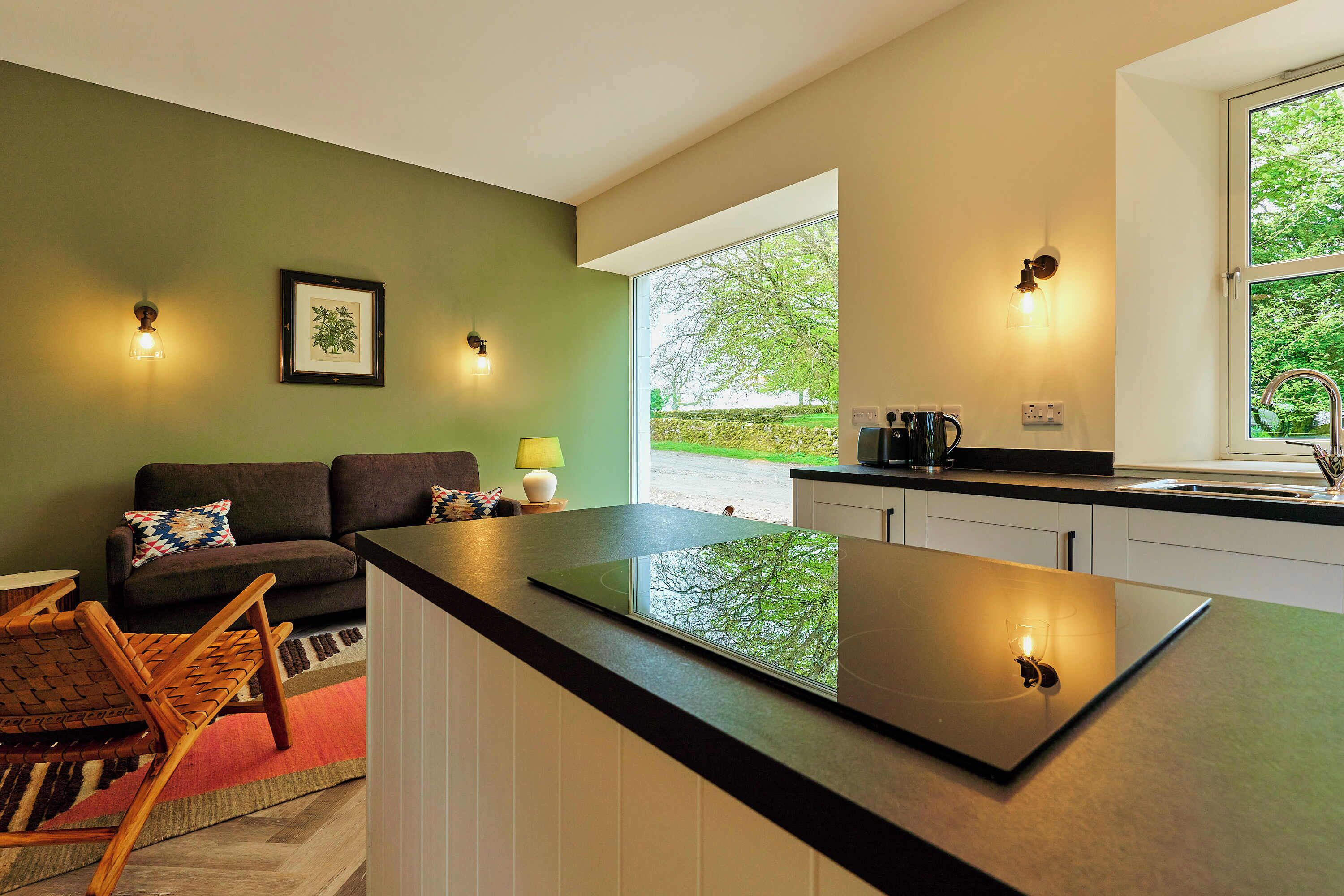 A modern kitchen with a black countertop, white cabinets, and a window providing a view of greenery outside.