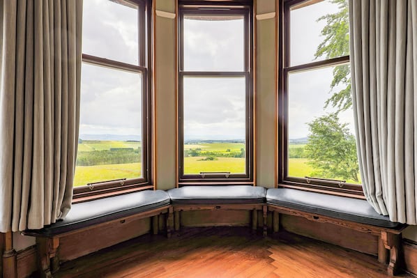 A corner bay window with a view of a green landscape.