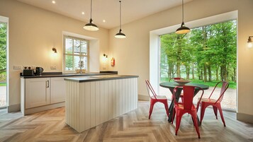 Una cocina moderna con una isla central, un comedor con sillas rojas y ventanas grandes que dan a vistas de árboles.