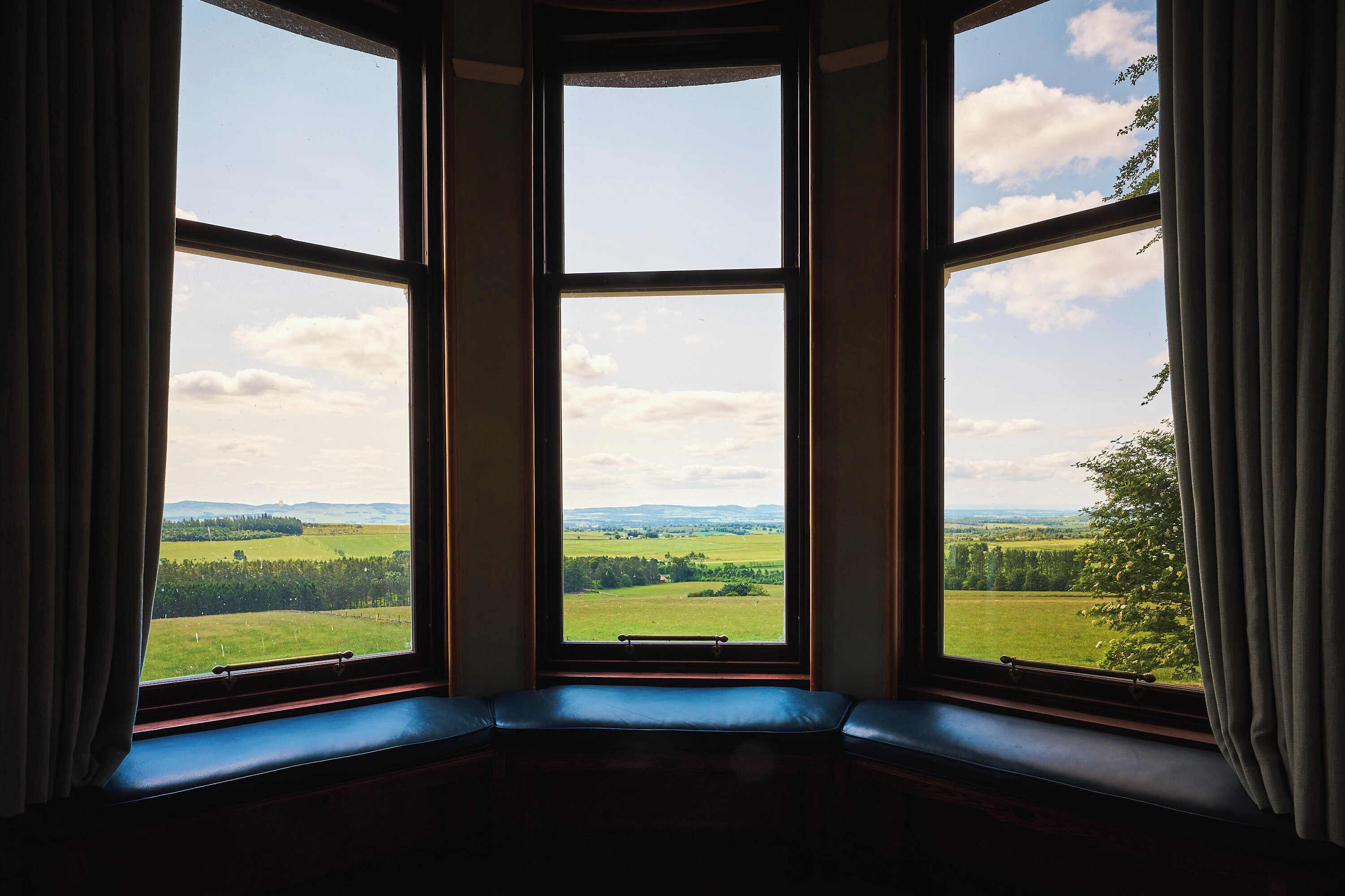 A room with a bay window overlooking a green landscape.