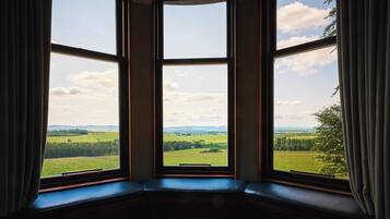 A room with a bay window overlooking a green landscape.