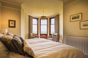 Una habitación de hotel con una cama grande, dos sillas, una mesa y vistas al campo a través de amplios ventanales.