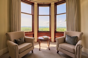 Una habitación con dos sillones, una mesita y un ventanal con vistas a un paisaje verde.
