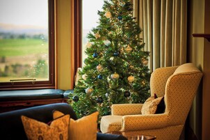 A cozy living room with a Christmas tree, a patterned armchair, and a view of a green landscape through a window.