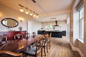 A dining area with a wooden table and chairs, a kitchen in the background, and pendant lighting. - Kinclune House, Estate & Cottages (Kirkton of Kingoldrum)