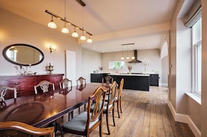 Un comedor con mesa y sillas de madera, una cocina al fondo e iluminación colgante.