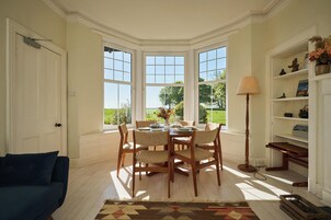 Un comedor con una mesa preparada para cuatro personas, rodeada de sillas, con vista a un jardín a través de ventanas amplias.