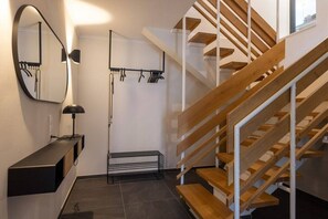 Ein modernes Interieur mit einer Holztreppe, einem schwarzen Konsolentisch und einem an der Wand befestigten Spiegel.