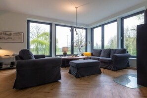 Un salon moderne avec de grandes fenêtres, un ensemble de canapés, une table basse et une lampe.