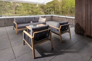 Ein Sitzbereich im Freien mit einer Couch und zwei Sesseln, einem kleinen Tisch und einer Holzterrasse.