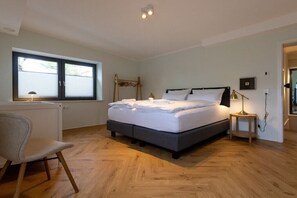Une chambre à coucher comprenant un lit, une table de chevet, une lampe, une chaise et une fenêtre avec des stores.