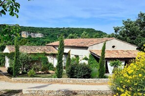 Un edificio tradizionale con tetto in tegole, circondato da vegetazione e un muro in pietra.