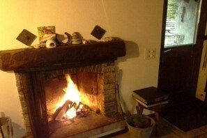 A fireplace with a mantel decorated with various items, a fire burning inside, and a window to the right. - Holiday home in Gerra with barbecue (Gerra)