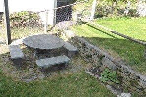 A stone table with benches in a garden area with a stone wall and a chain-link fence. - Holiday home in Gerra with barbecue (Gerra)