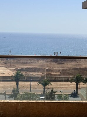A view of a coastal area with a sandy beach, a road with vehicles, and a clear sky. - Elegant 3 bed apartment with sea view (Anza)