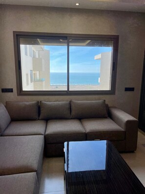 Ein modernes Wohnzimmer mit großem Fenster, einem Ecksofa und einem Glastisch.