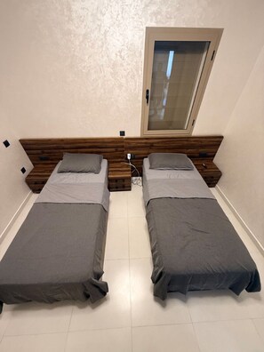 A twin room with two single beds, a wooden headboard, a small window, and a white tiled floor. - Elegant 3 bed apartment with sea view (Anza)