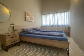A bedroom with a bed, bedside table, lamp, and a window with curtains. - Holiday home with 3 bedrooms (Cadzand-Bad)