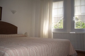 A bedroom with a bed, a nightstand, a window with curtains, and a radiator. - Holiday apartment with 1 bedroom (Cavaillon)
