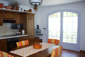 A kitchen with wooden cabinets, a stove, a dining table with chairs, and a television. - Holiday apartment with 1 bedroom (Cavaillon)