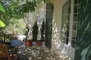 An outdoor patio with a table and chairs, potted plants, and a window with a view of greenery. - Holiday apartment with 1 bedroom (Cavaillon)