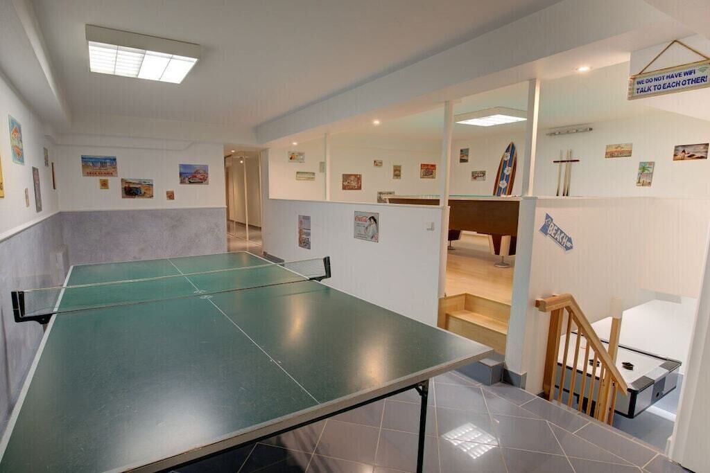Ein Zimmer mit einem Tischtennis-Tisch, einer Holztreppe und verschiedenen gerahmten Bildern an den Wänden.