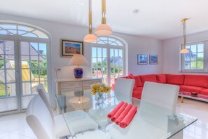 Ein moderner Essbereich mit einem Glastisch, weißen Stühlen und einem roten Sofa.
