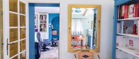A room with a mirrored wall, a wicker chair, a bookshelf, and a door leading to another room.