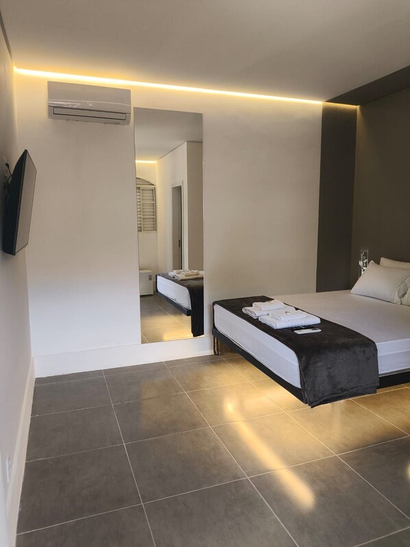Una habitación de hotel moderna con cama, mesita de noche y televisor de pantalla plana montado en la pared.