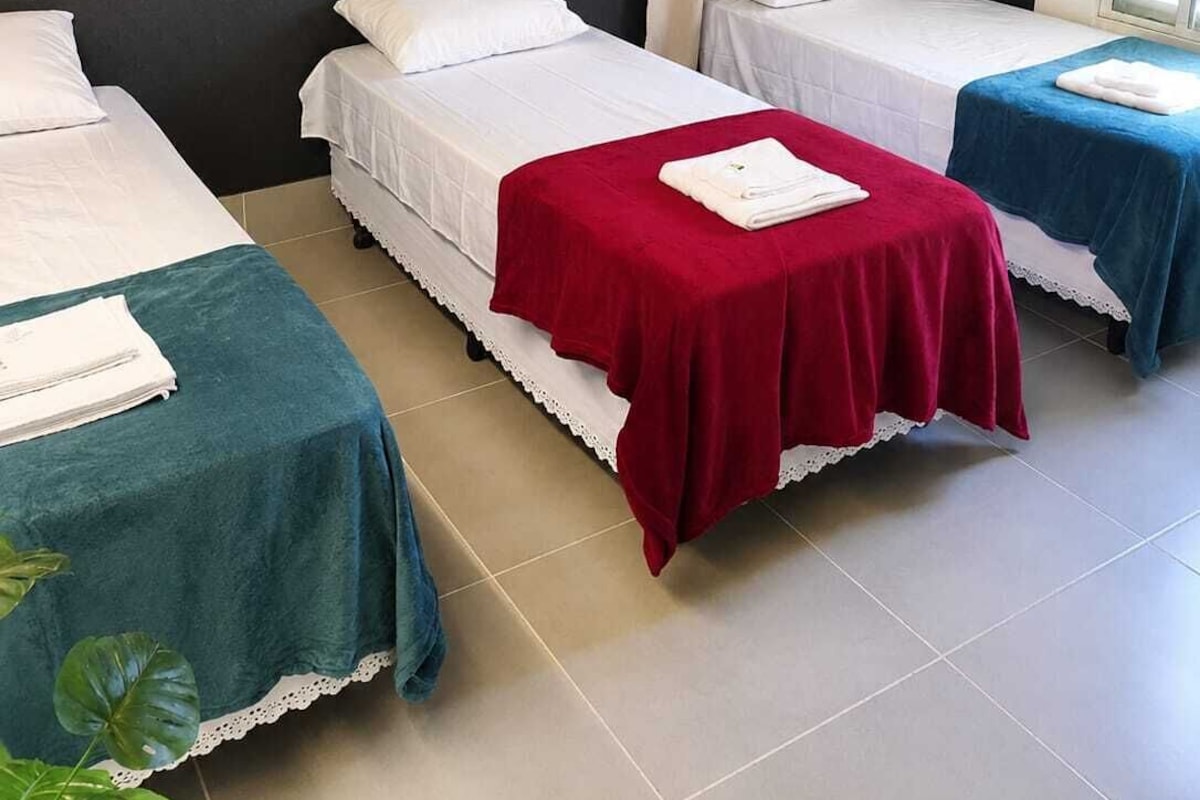 A hotel room with three single beds, each with a different colored bedspread.