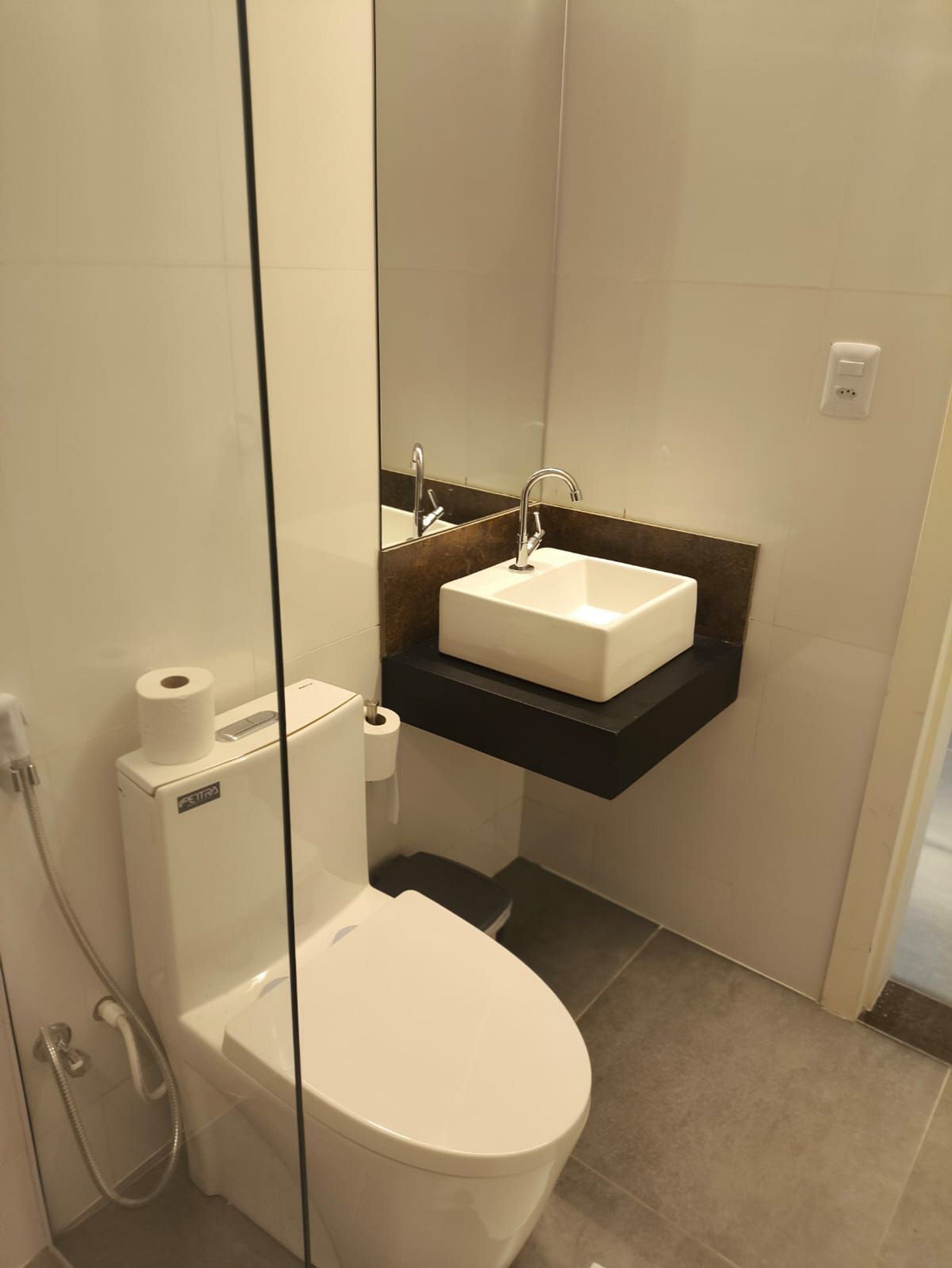 A modern bathroom with a white toilet, a glass-enclosed shower, and a white sink with a black countertop.