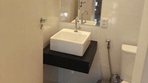 A bathroom with a white sink, a black countertop, a mirror, and a toilet. - Gyn Suites (Goiania)