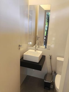 A bathroom with a white sink, a black countertop, a mirror, and a toilet. - Gyn Suites (Goiania)