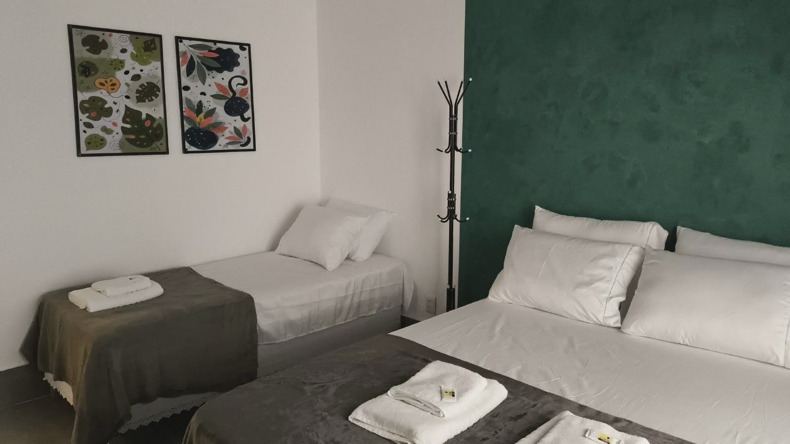 A hotel room with two beds, a green accent wall, and a coat rack.