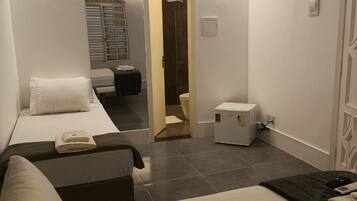 Quarto de hotel com cama, mesinha de cabeceira, escrivaninha e cadeira. Um banheiro é visível por uma porta aberta.