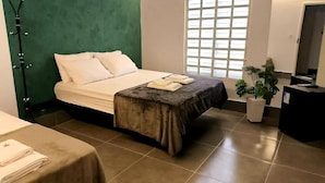 A hotel room with a bed, a small table with towels, a potted plant, and a desk with a computer. - Gyn Suites (Goiania)