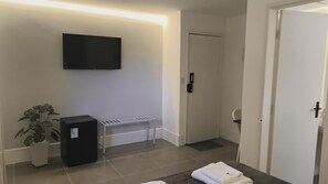 A modern bathroom with a flat-screen TV mounted on the wall, a small black cabinet, a white towel rack, and a potted plant. - Gyn Suites Sul (Goiania)