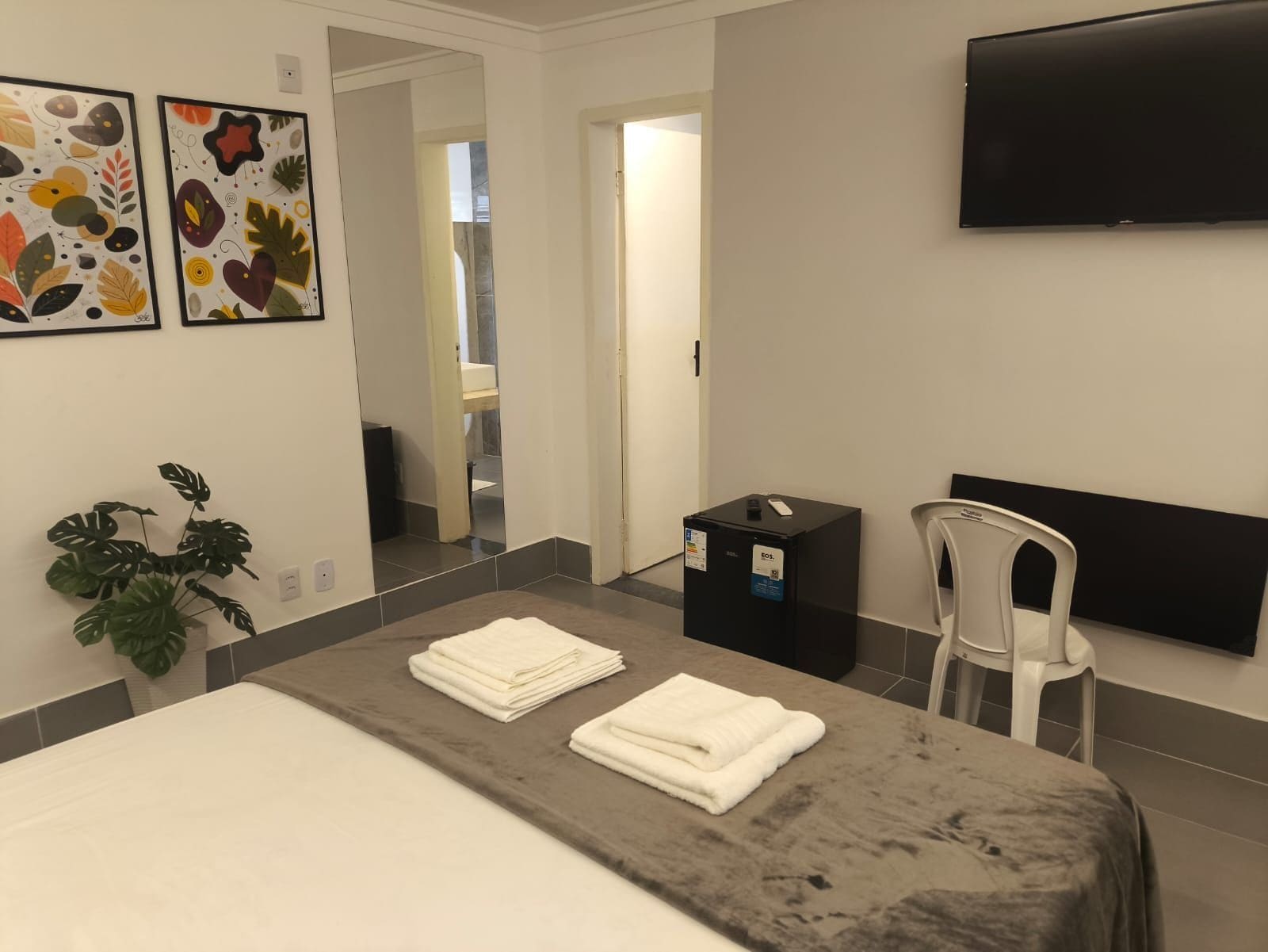 Habitació d'hotel amb un llit, una taula, una cadira, una televisió i obra d'art a la paret.