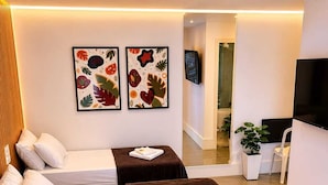 A hotel room with two beds, a TV, a plant, and artwork on the wall. - Gyn Suites (Goiania)