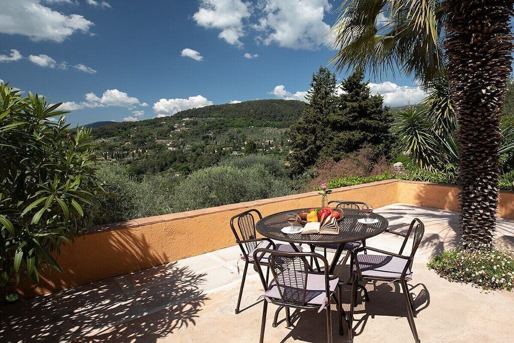 An outdoor patio with a round table and chairs, overlooking a scenic landscape with hills and trees.