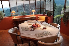A dining area with a table set for four, a view of the outdoors, and a window with blinds. - Villa in Grasse with swimming pool (Grasse)