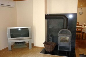 A room with a television on a stand, a fireplace with a chimney, and a wicker basket on the floor. - Holiday home with 1 bedroom (Vimmerby - Hyltabyn)